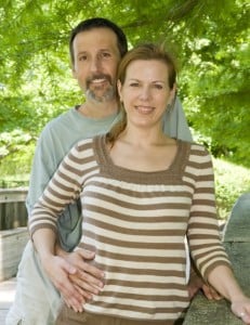 A man and a woman stand in front of green trees in a park.