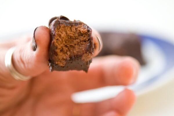 A hand holds a bite-sized vegan 3 Muskateers Bars with a bite taken out of it.