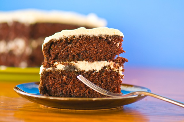 Slice of Vegan Suzy Q Cake on a plate with a fork resting on the plate and a bright blue background