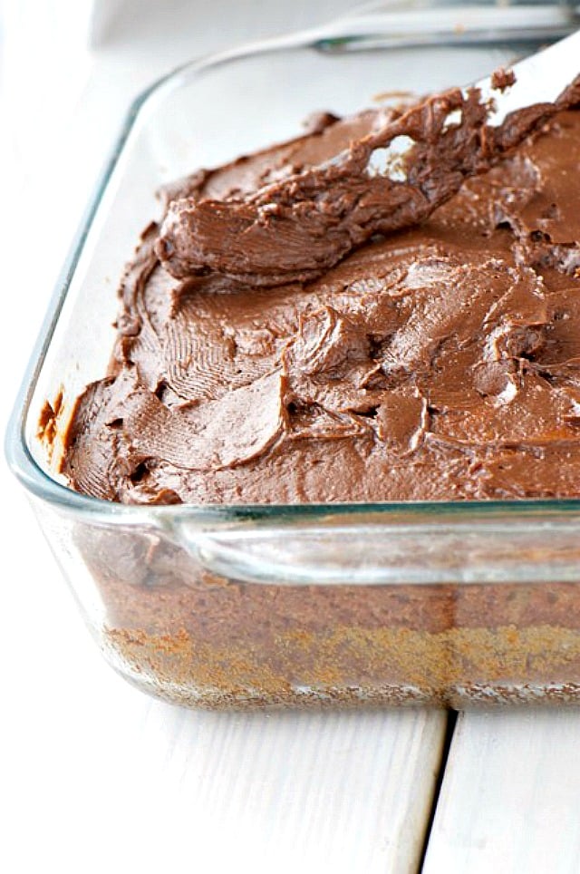 A knife is spreading chocolate frosting over a cake.