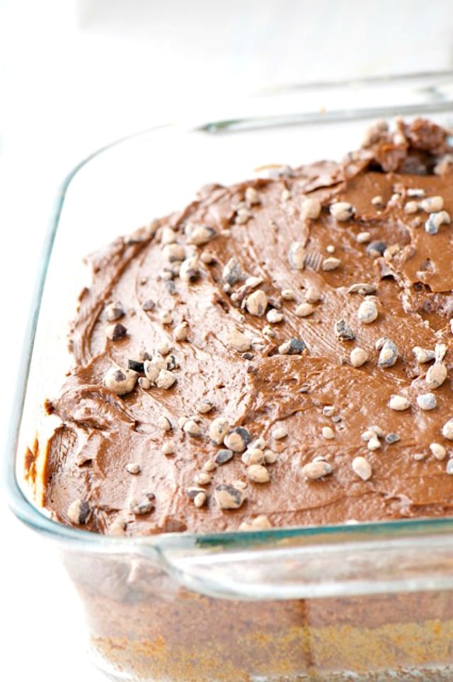 Chocolate frosted cake in a 9X13 baking dish has chocolate cacao nibs sprinkled on top.