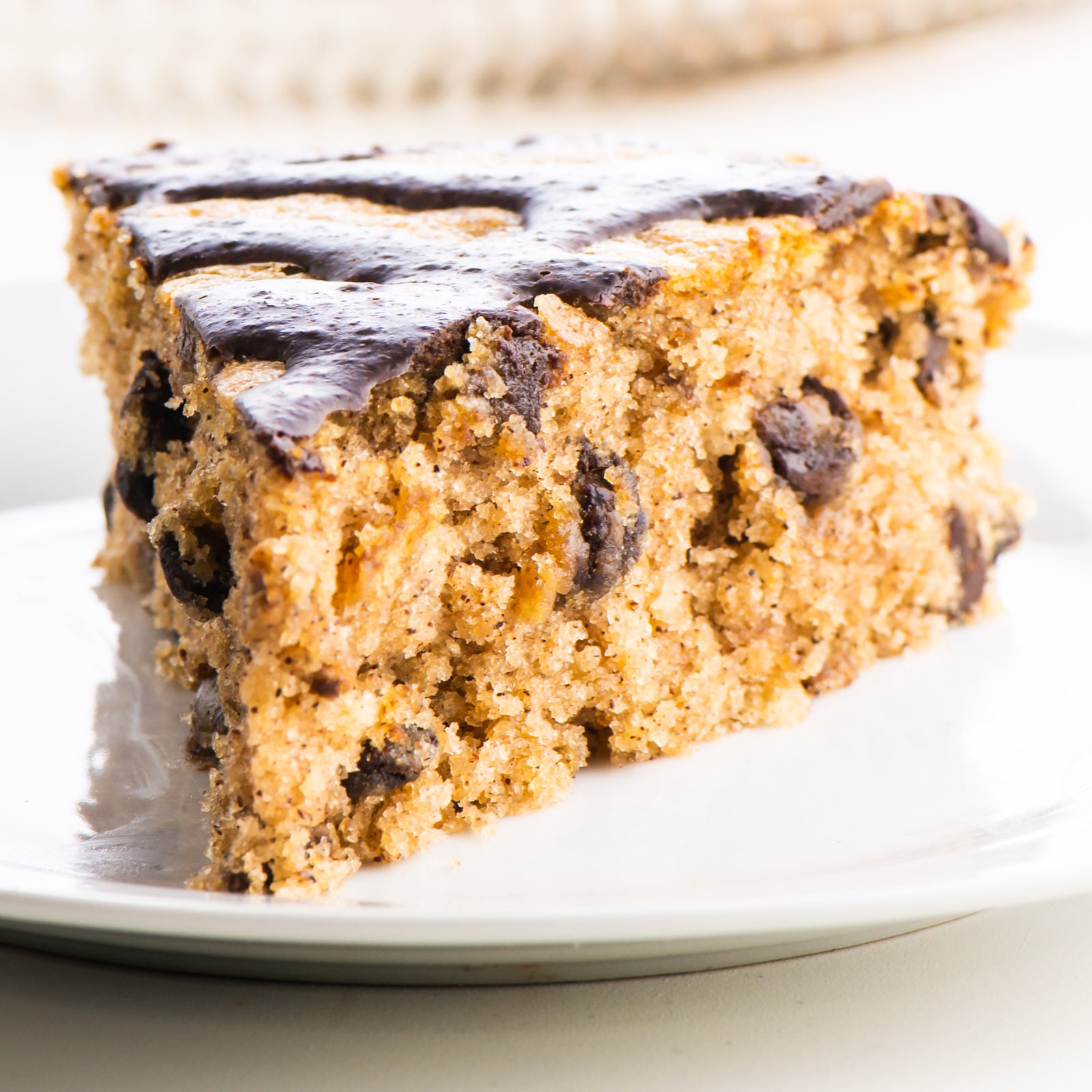A slice of almond butter cake sits on a plate. It's topped with chocolate drizzles.