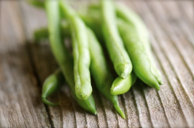 A photograph of raw green beans on an old wood table top.
