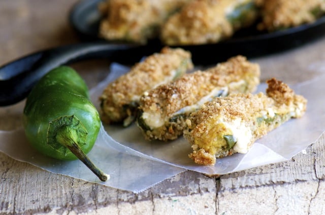 Three baked jalapeño poppers sit next to a fresh jalapeño. 