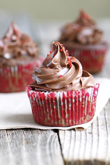 Three Chocolate cherry cupcakes sit on a napkin on a wooden table.