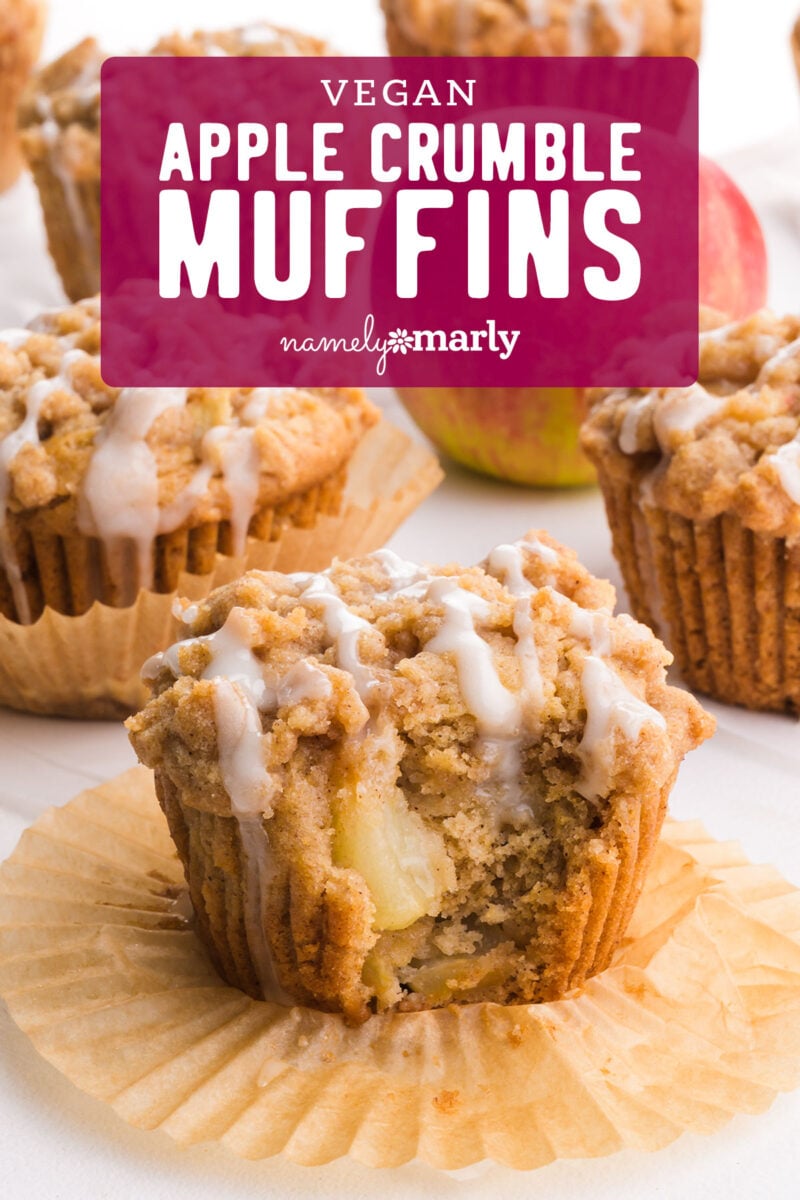 Vegan apple crumble muffins topped with icing, placed on parchment paper with fresh apples in the background.