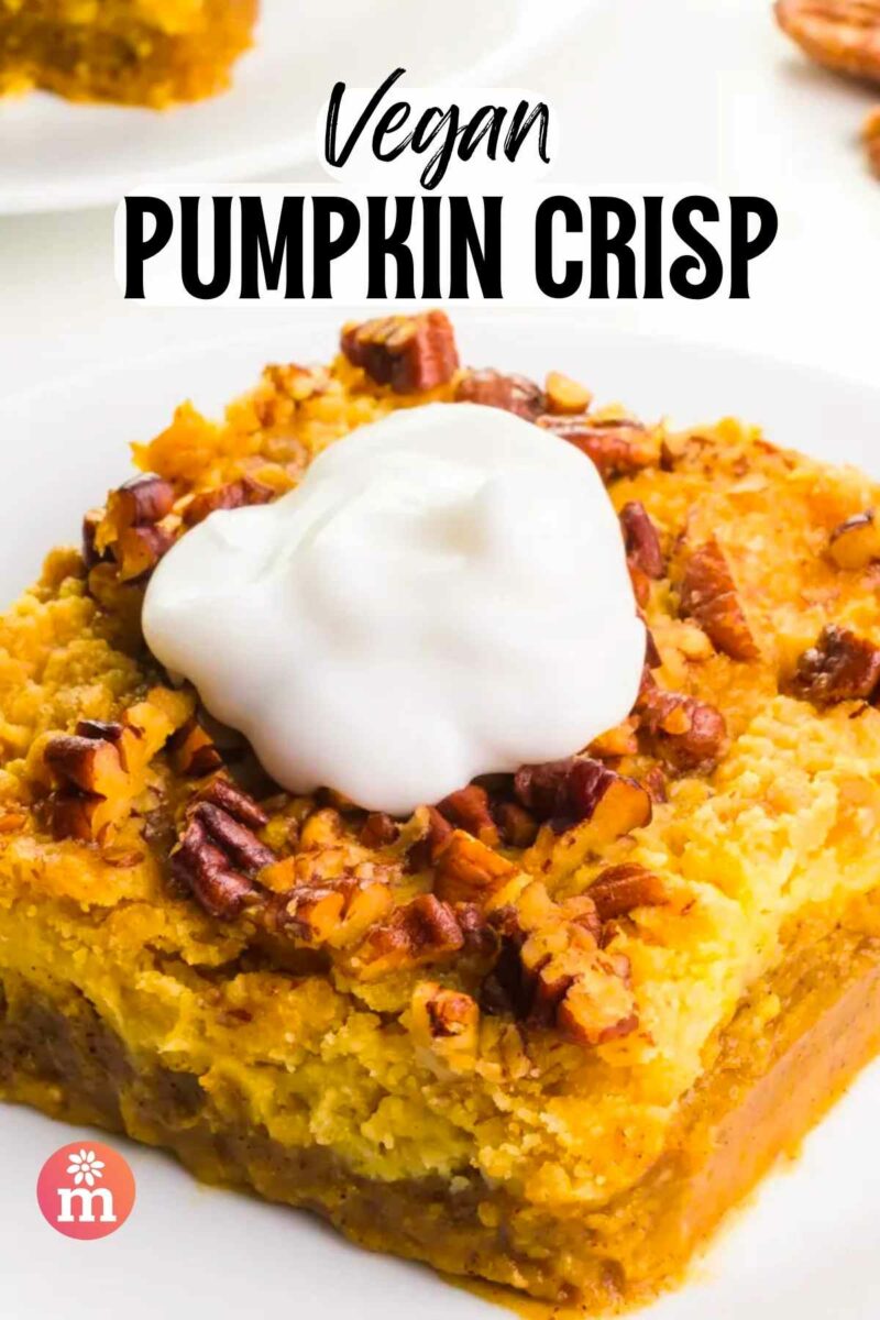 Vegan pumpkin crisp topped with whipped cream and pecans on a white plate.