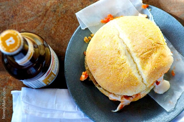 Overhead view of a Veggie Chicken Parmesan Sandwich on a plate next to a bottle of beer