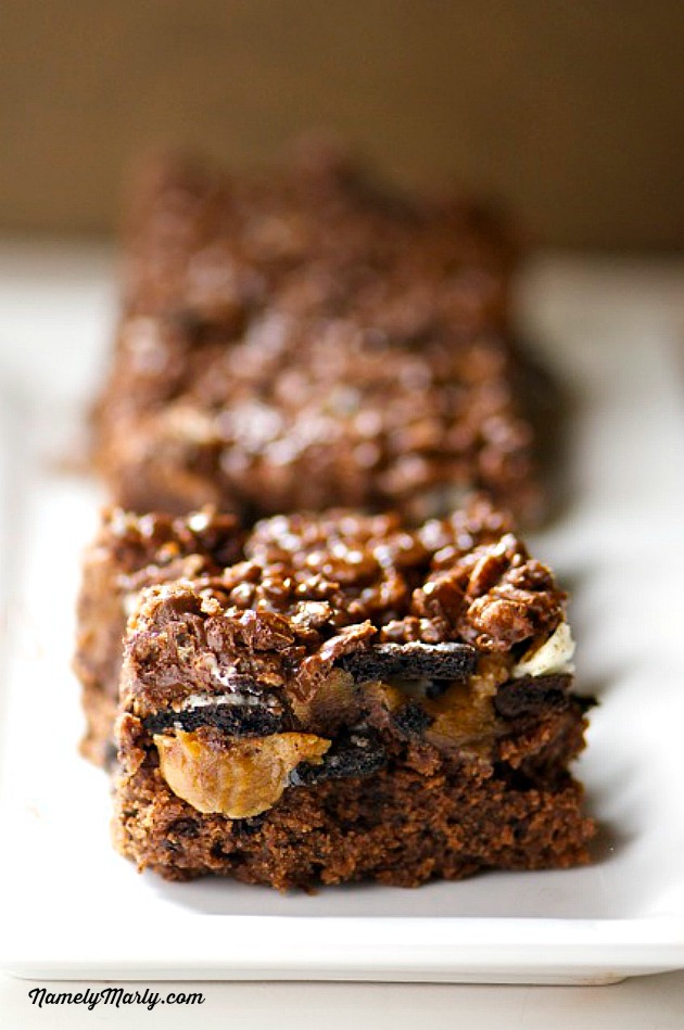 A row of layered brownies sits on a serving dish. There are bits of peanut butter and Oreo cookies showing through the layers.