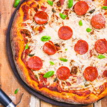 Looking down on a vegan pizza on a wooden counter with a pizza cuter next to it.