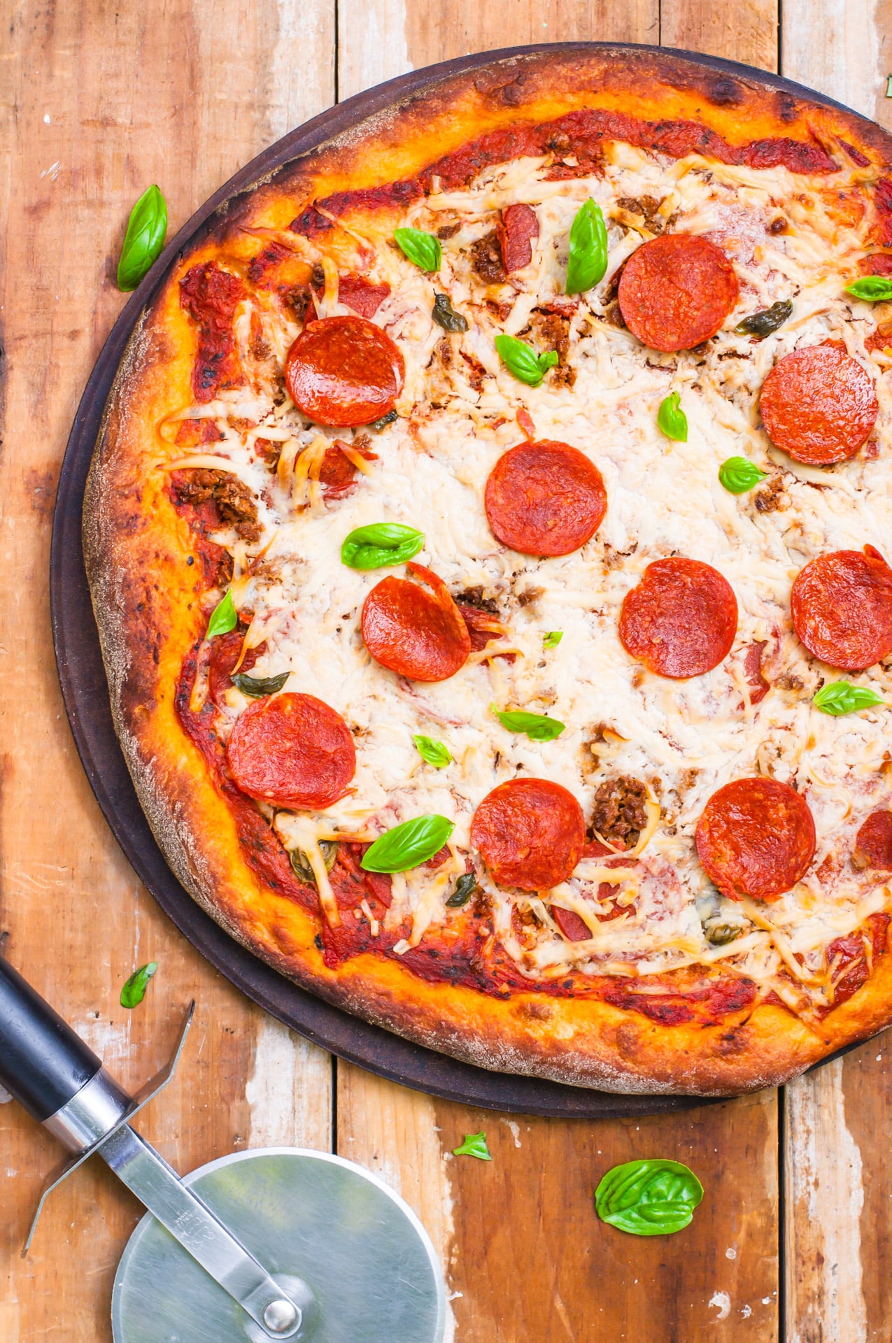 Looking down on a vegan pizza on a wooden counter with a pizza cuter next to it.