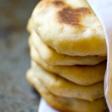 A stack of baked Naan Bread is nestled in a white kitchen cloth napkin.