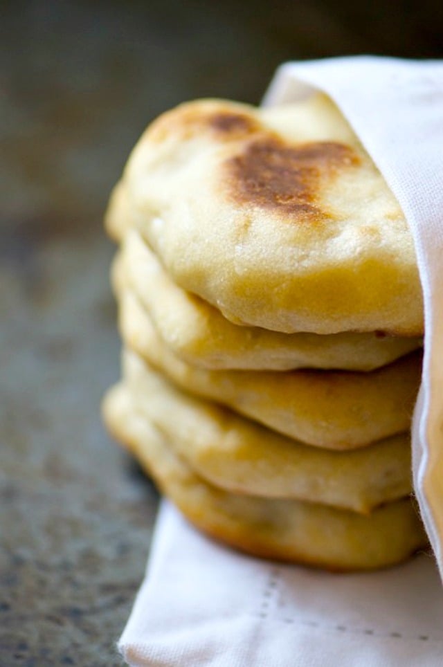 A stack of baked Naan Bread is nestled in a white kitchen cloth napkin.