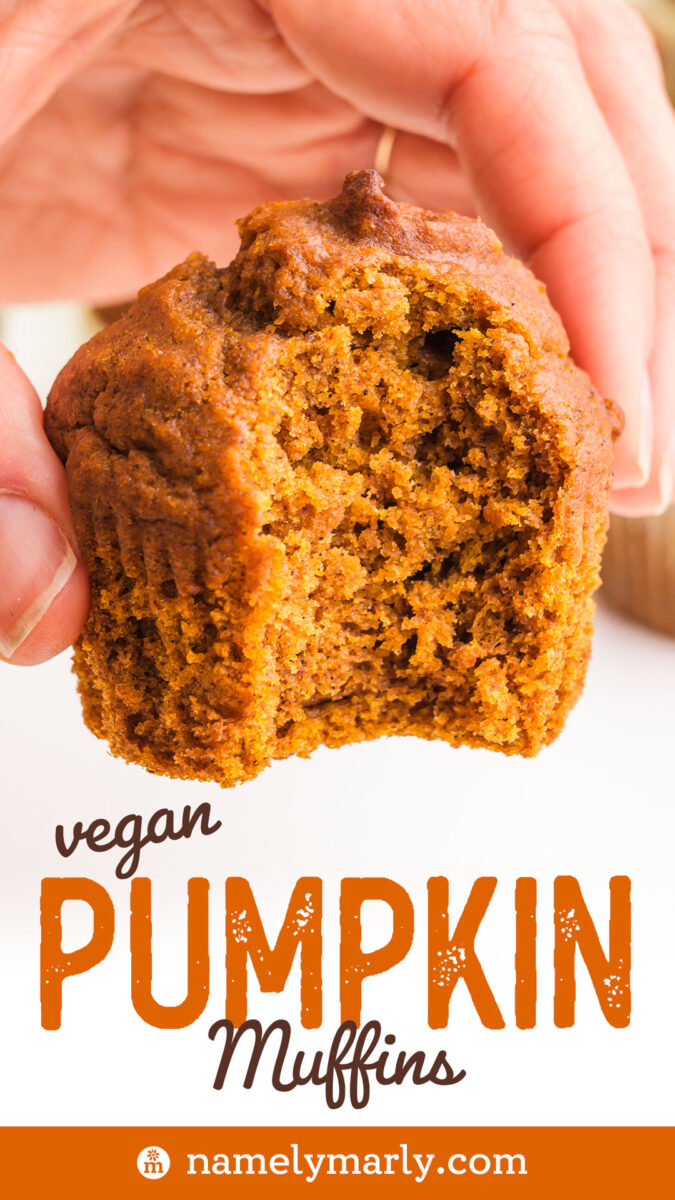 A hand holds a bitten vegan pumpkin muffin, with a soft texture and orange-brown color.