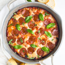 Pizza dip is in a skillet and is topped with pepperoni and basil leaves.