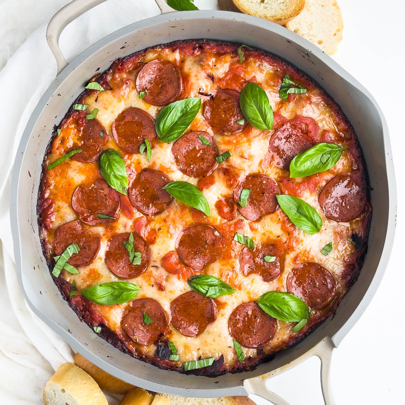 Pizza dip is in a skillet and is topped with pepperoni and basil leaves.