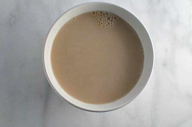 A white bowl sits on a white counter and has liquid in it, the beginnings of the cake batter.