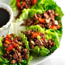 A platter of lettuce wraps filled with veggie filling and sitting next to a bowl of dipping sauce.