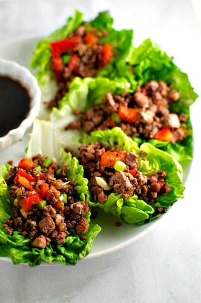 A platter of lettuce wraps filled with veggie filling and sitting next to a bowl of dipping sauce.