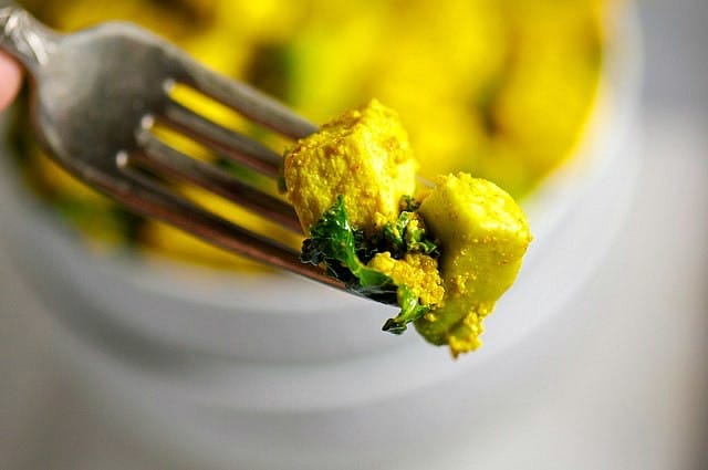 A fork holds a bite from a tofu breakfast bowl showing bits of tofu, kale and avocados on a fork.
