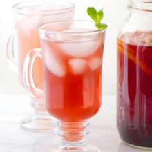 Two tall glasses with ice and punch inside, one with a mint sprig at the top are sitting next to a mason jar full of punch.