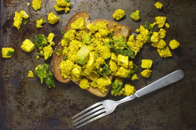Looking down on a slice of toast with Avocado Kale Tofu Scramble on top if it and around it. A fork is below it.