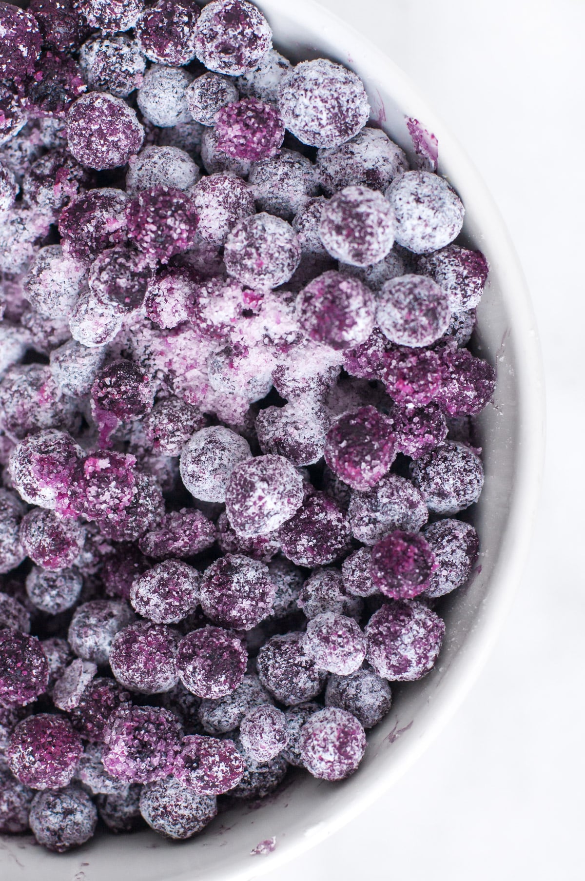 Blueberries covered with sugar and cornstarch in a white bowl.