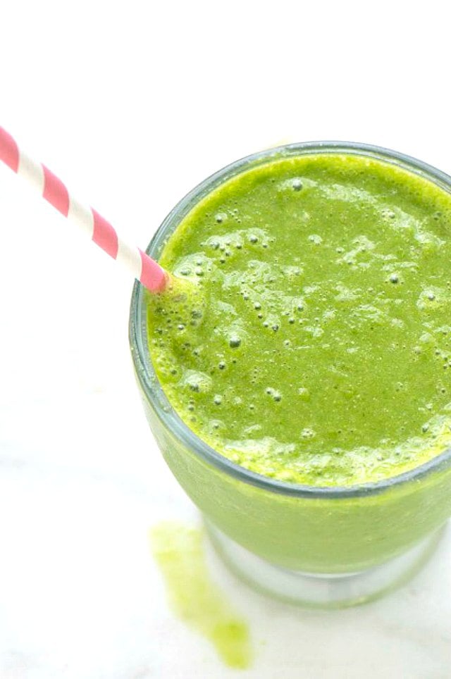 Looking down at a glass full to the rim with a green drink with a pink paper straw.