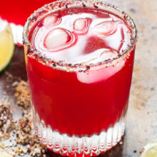 Two glasses of Hibiscus Margaritas with lime wedges around them.