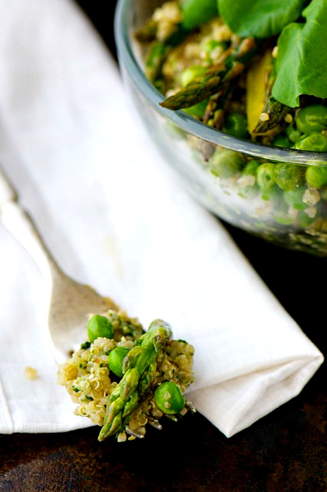 A closeup of a fork on a white napkin. The fork holds a bite of quinoa pesto with asparagus. The bowl with the rest of the meal sits next to it.