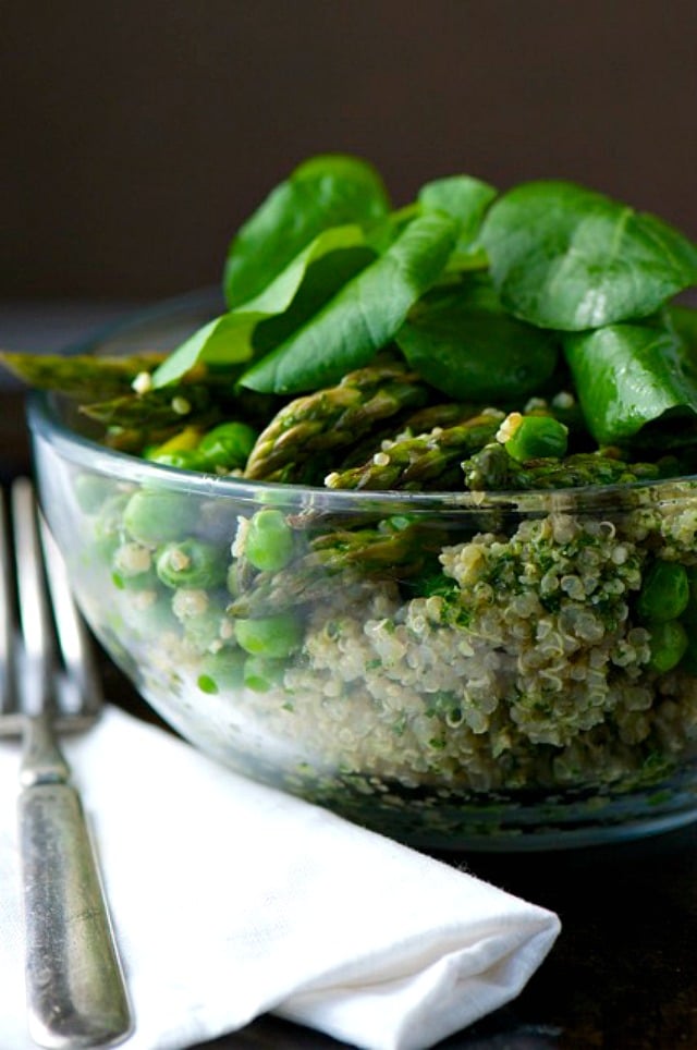 A closeup of a bowl of a Quinoa Pesto Veggie Bowl with fresh spinach on top.