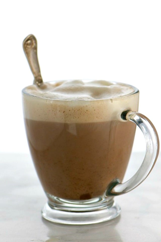 A glass mug full of hot cocoa with lots of frothy plant based milk at the top.