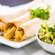 Vegan chicken taquitos are on a plate next to guacamole.