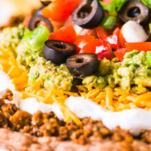 A close-up shot of vegan 7 layer dip shows layers of beans, veggie crumbles, and more toppings.