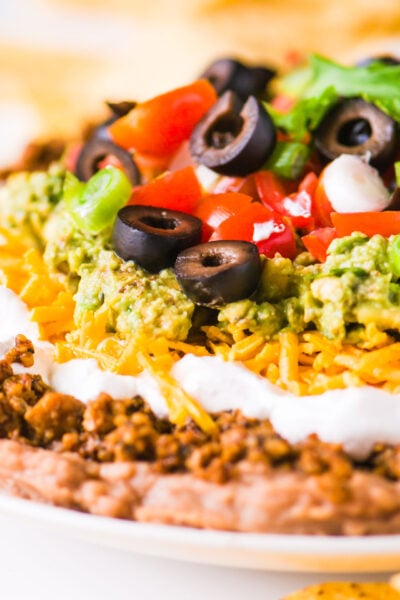 A close-up shot of vegan 7 layer dip shows layers of beans, veggie crumbles, and more toppings.