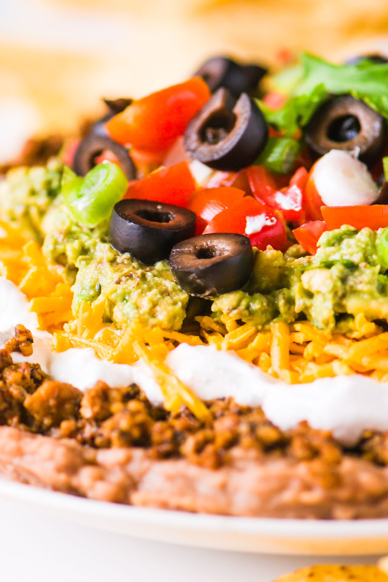 A close-up shot of vegan 7 layer dip shows layers of beans, veggie crumbles, and more toppings.