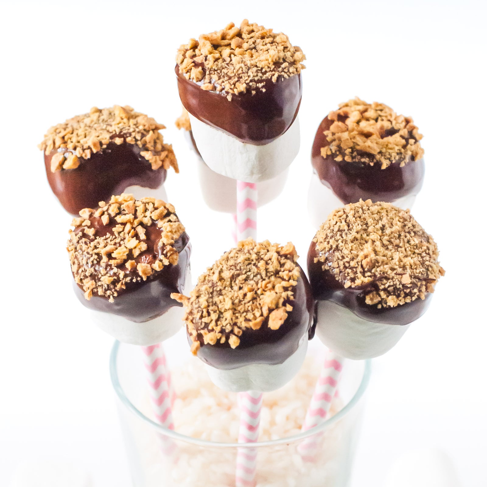 Several Vegan Marshmallow Pops in a tall glass filled with uncooked brown rice.