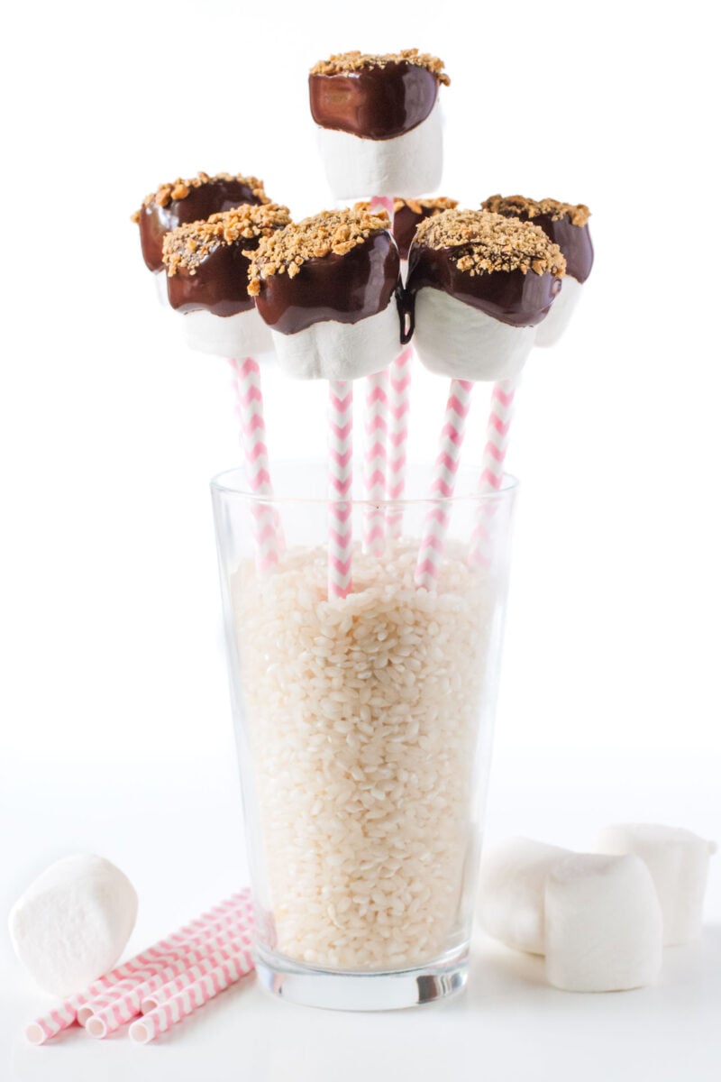 Several Vegan Marshmallow Pops in a tall glass filled with uncooked brown rice.
