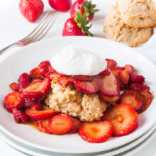 A plate of Vegan Strawberry Shortcake surrounded by sliced strawberries and topped with vegan whipped cream.
