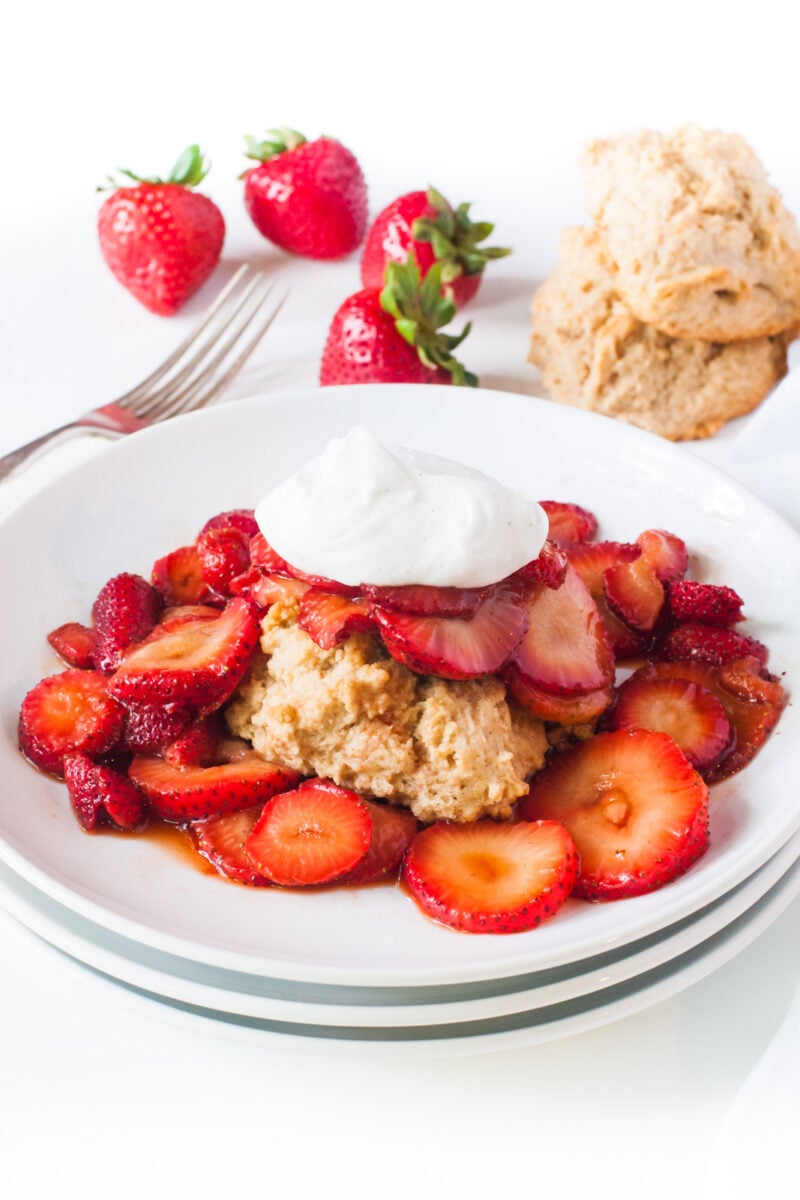 A plate of Vegan Strawberry Shortcake surrounded by sliced strawberries and topped with vegan whipped cream.