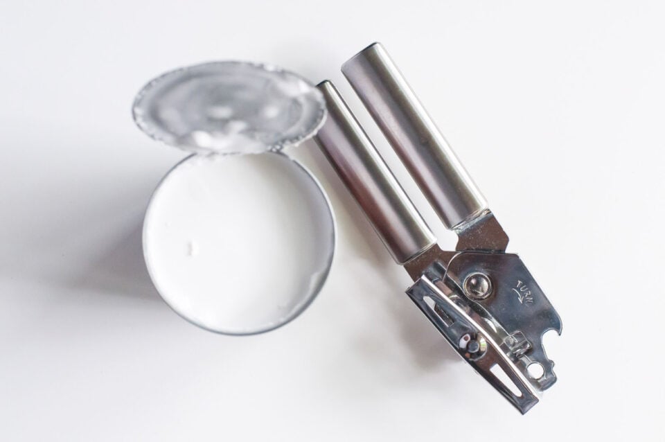 A opened can of coconut milk sits next to a can opener.