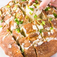 A hand pulls out a piece of cheesy vegan pull-apart bread.
