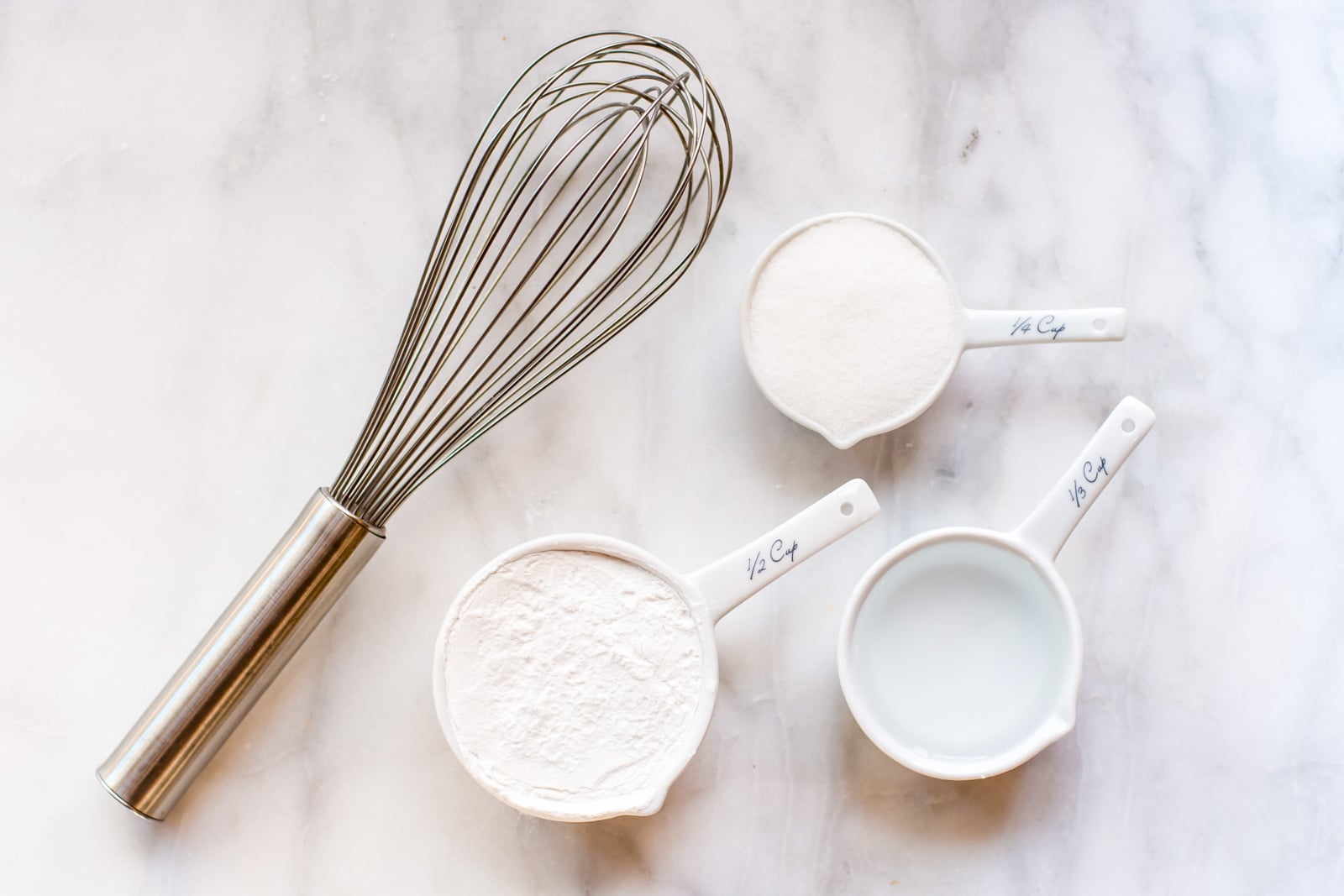 Looking down on some ingredients in measuring cups, like sugar, and water.