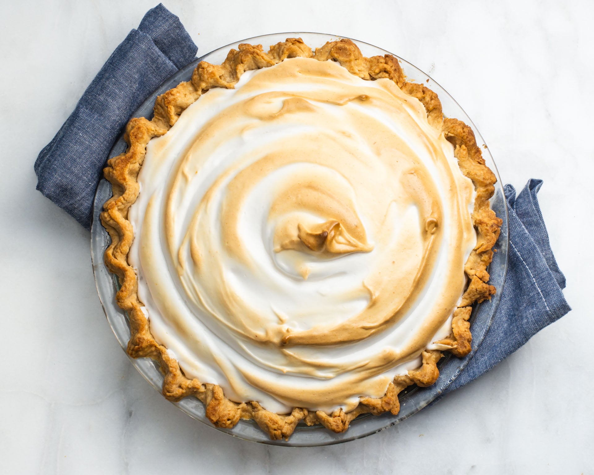 Looking down on a pie with a baked meringue on top with golden peaks. There's a blue kitchen towel below it.