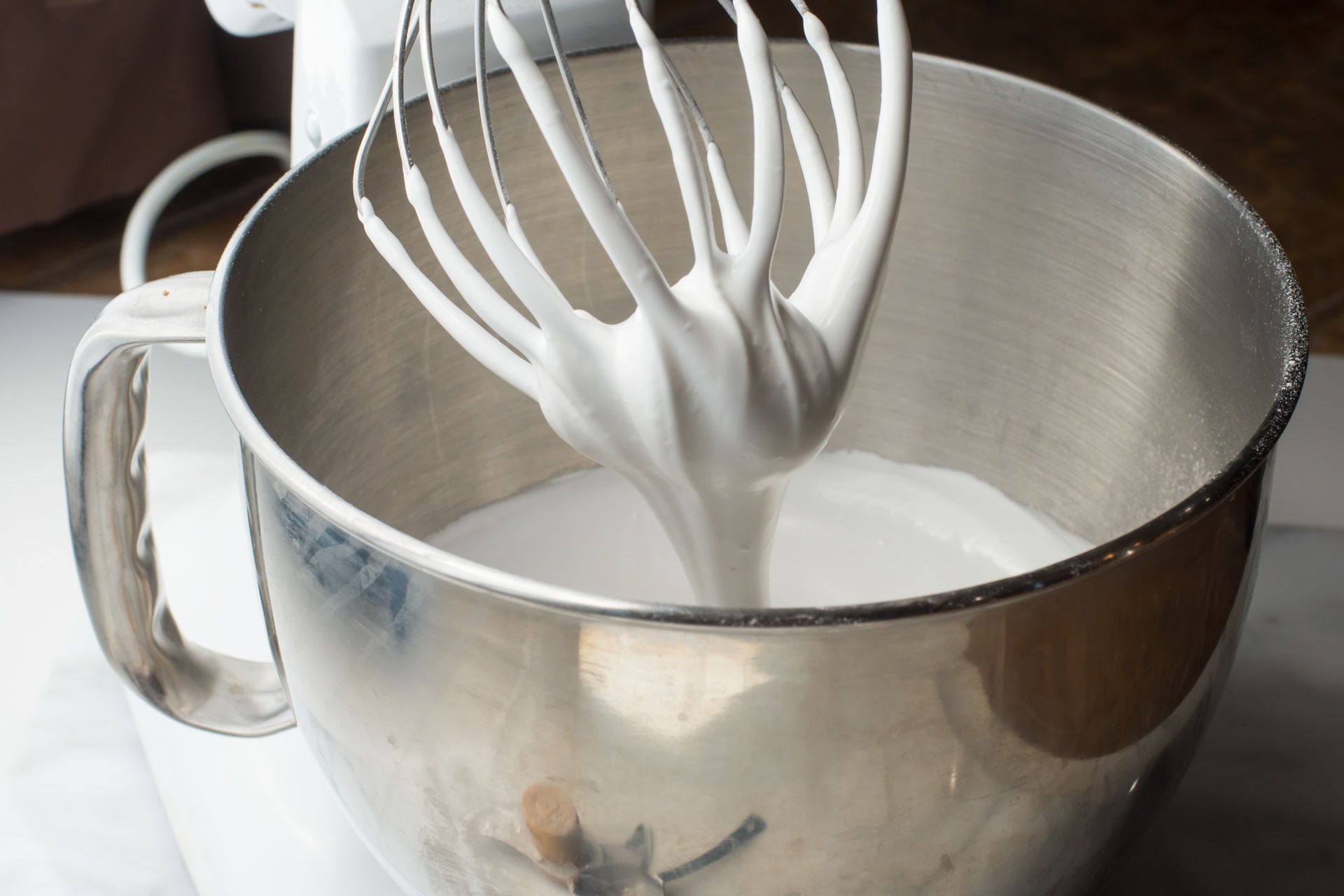 A stand mixer has been pulled back and the vegan meringue is thickly falling from the beaters.