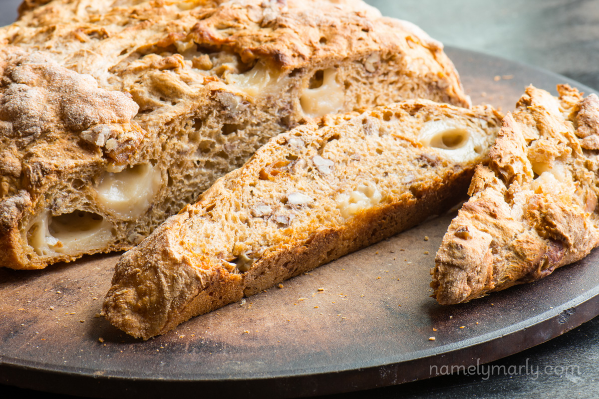 A rustic loaf of bread on a pizza stone, with a couple of slices cut off.