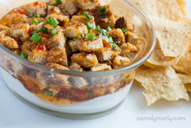 Looking down on vegan dip in a bowl, topped with crispy tofu pieces and green onions. There are tortilla chips beside it.