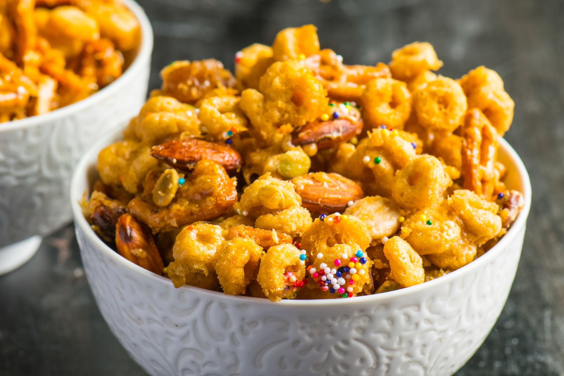 One bowl of Cheerio snack mix sits in front of another bowl.