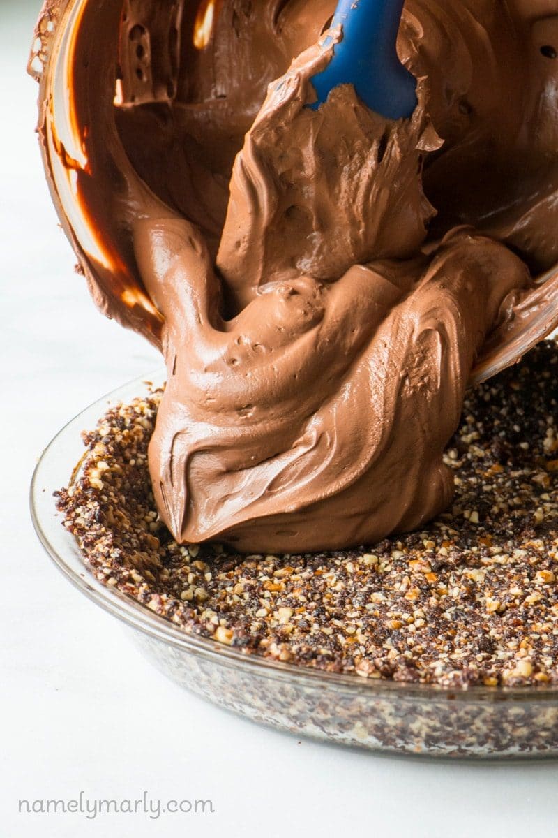 A spatula is spooning out the chocolate pudding into the prepared pie crust.
