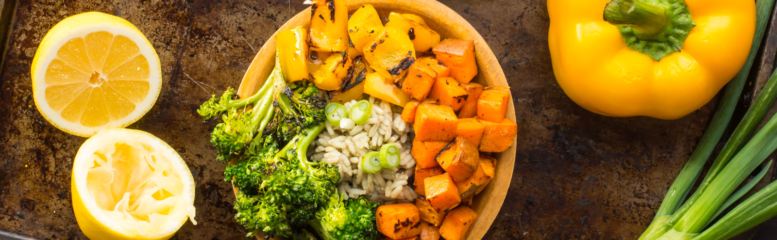 Overhead view of a bowl of fried vegetables sitting next to a sliced lemon and yellow bell pepper